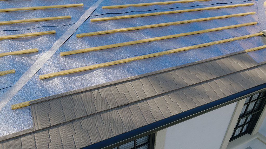 Close-up of a roof under construction with reflective insulation and wooden battens installed over the shingles.